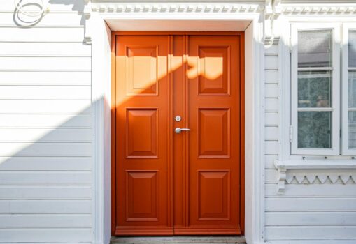 A vibrant orange door on a white wooden house, featuring classic architectural details.